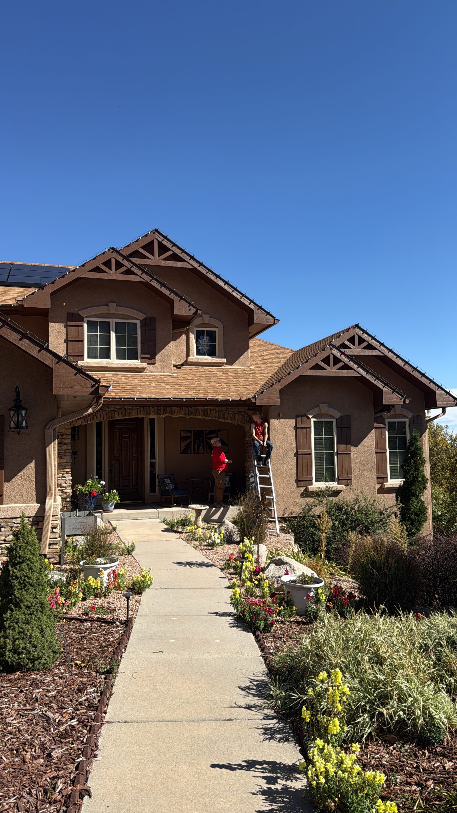 Christmas light installation in progress on a tan stucco two-story residential home