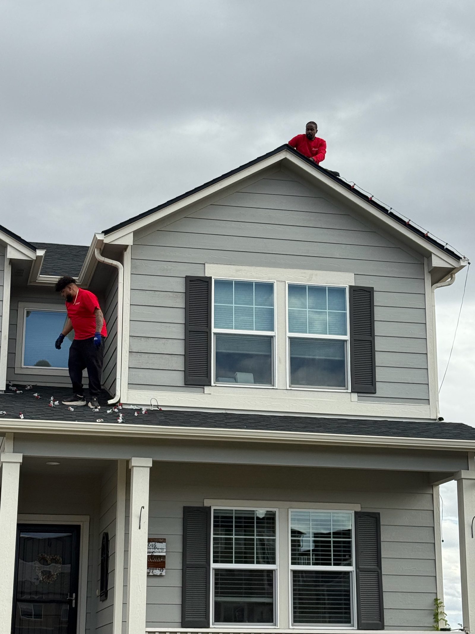 Our installers on roof peak hanging holiday lights on a gray Front Range house