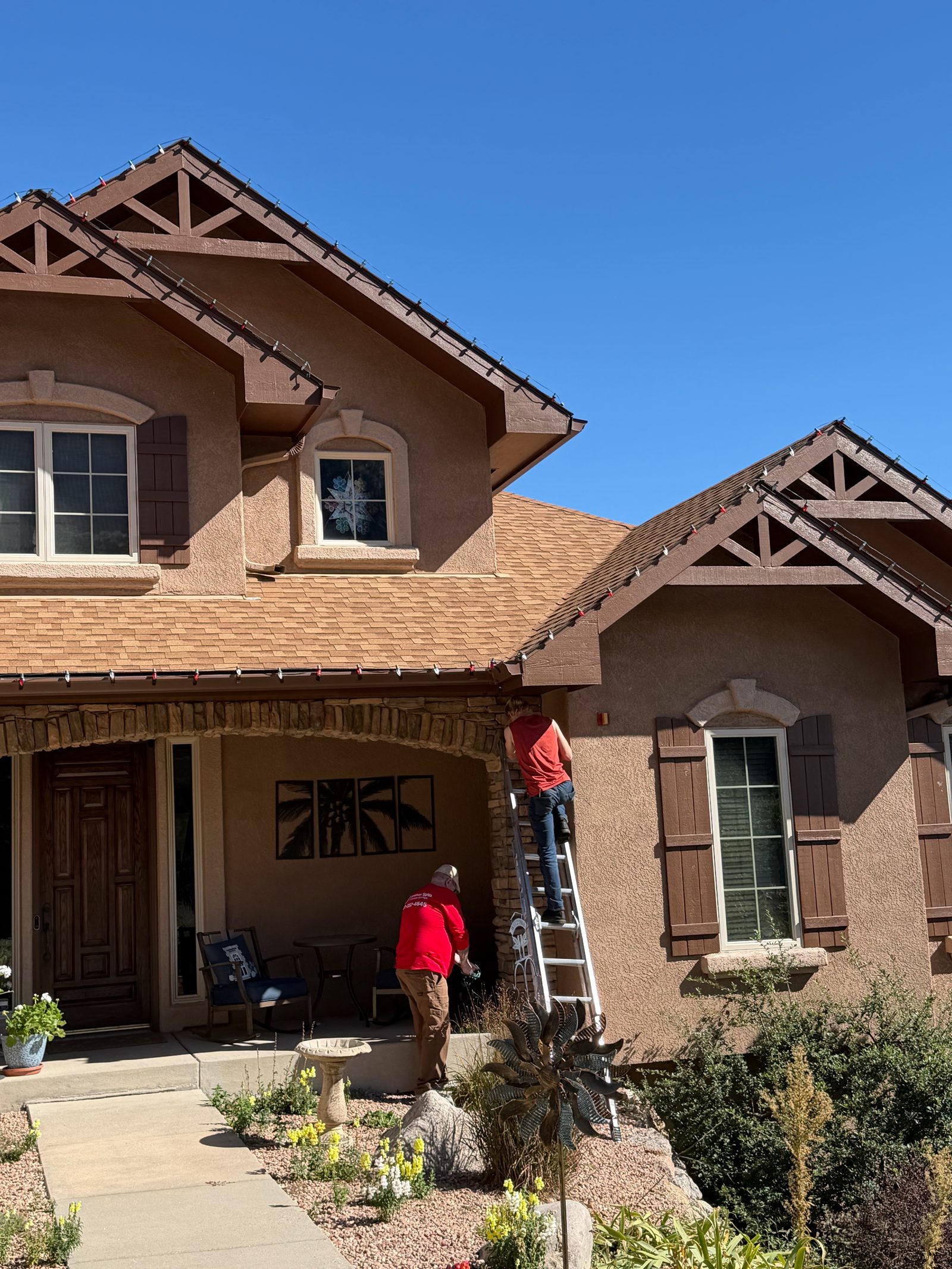 Our crew on ladder installing roofline Christmas lights by the front porch