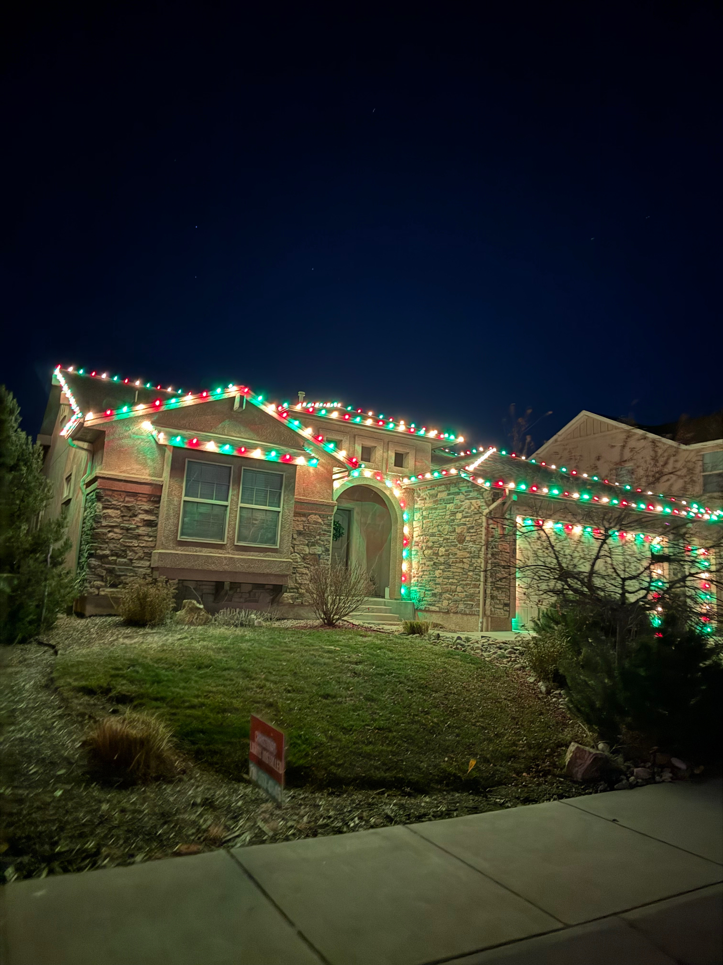 Multicolor Christmas lights on a two-story Front Range home with roofline and landscape holiday lighting